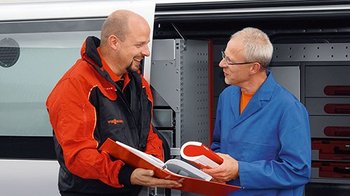 Zwei Männer im Gespräch über Werkzeuge im Lieferwagen Ein Vissmann Mitarbeiter zeigt einem Kunden, einen Ordner vor einem Firmenbulli